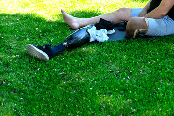 A prosthetic leg lies next to a white man, sitting on the grass, lawn. Rehabilitation, leg amputation