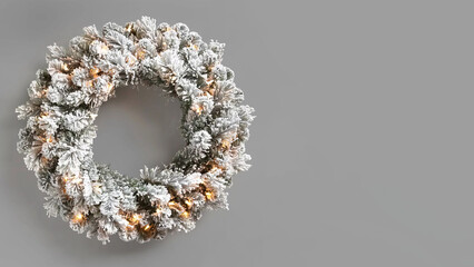 Christmas wreath with flocked greenery and led lights on grey copy-space background.