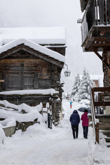 two person in the snow covered house walking a dog in a old wooden mountian village in Switzerland