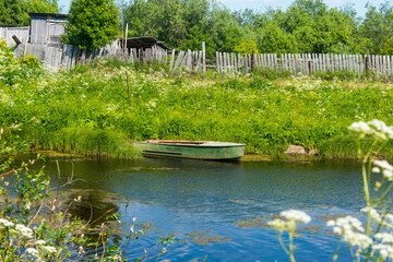 a metal rowing boat moored to the shore of the lake against the background of grass and an old...