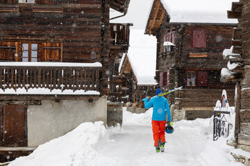 A skier walks down the snowy alley of an old mountain village in the Swiss Alps - 687252398