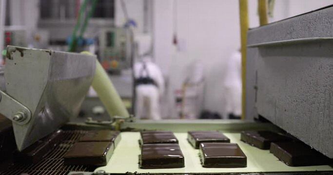 Industrial ice cream dessert factory.  Closeup view of a conveyer belt transporting ice cream tablets coated with chocolate by an automated machine. 