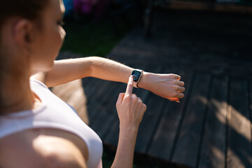 High-angle view of sporty female runner checking sports smart watch on summer sunny morning. Happy...