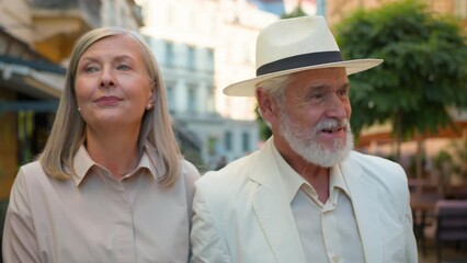 Smiling Caucasian happy family old couple elegant man gentleman woman lady pensioners tourists walk city street cafe restaurant talking discuss conversation outside retirement marriage holidays travel