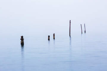 Old destroyed piles from a bridge into the sea in bad rainy weather