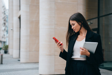 successful girl, lawyer stands outside courthouse, reads messages on phone, holds tablet and studies new information. Asian businesswoman waiting for  client to go to business meeting in office © Iona
