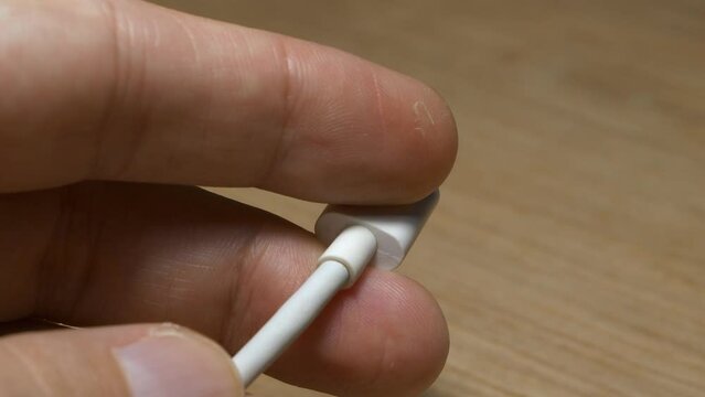 Hand inspecting used type-c cable jack on a wooden background. Close-up shot of fingers holding white USB-C cable, with dust and scratches all around the shell.