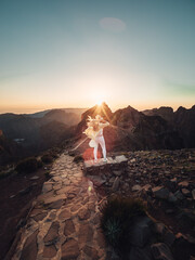 A daring adventurer basks in the warm glow of the madeira sunset, standing atop a rugged rock...