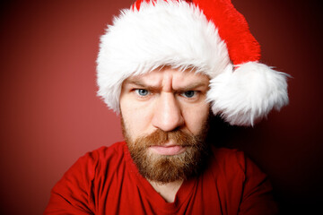 Naklejka premium Close Portrait of bearded Santa Claus in red hat, white beard with pensive emotion on red background