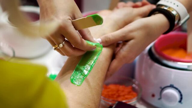 Carefully removing a strip of green sugaring paste from the hand of an adult woman in a beauty salon. The master runs his hand over the skin after depilation. Amateur hair removal procedure