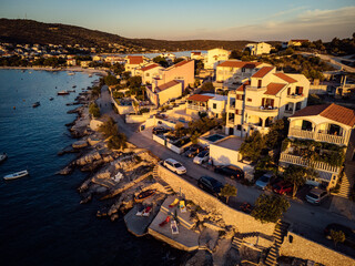 Amidst the tranquil landscape of a beachfront harbor, a row of colorful houses bask in the warm glow of a fiery sunset, as boats sway gently in the calm waters and the sky above transforms into a can