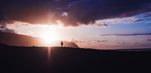 Amidst a breathtaking backdrop of vibrant skies and majestic mountains, a lone figure stands in...