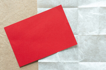 blank grungy red card positioned at an angle on tissue paper with crease marks on plain brown paper