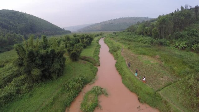 Aerial of Rwandan villagers walking along river path in rural mountainous countryside in Africa