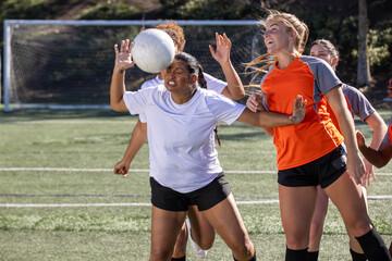 Female soccer players play in an intense and competitive game on the field outside. 