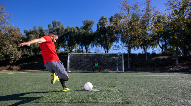 Soccer player kicking a free kick with the ball toward the goal. The goalie is waiting to block the kick during the game. 