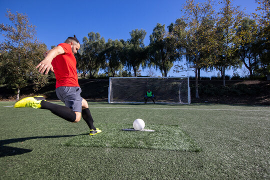 Soccer player kicking a free kick with the ball toward the goal. The goalie is waiting to block the kick during the game. 