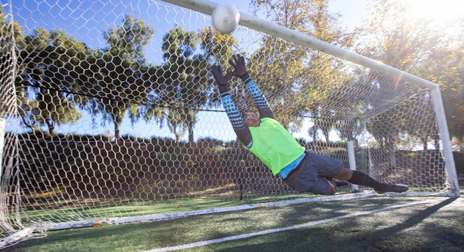 Athletic man attempts to block a goal. The soccer player is a goalie in front of the net during a game. 