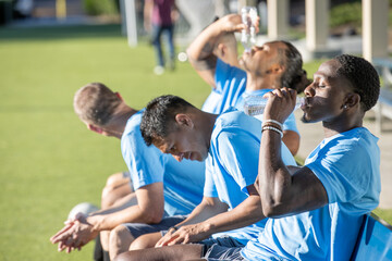 Soccer players cool off on a hot summer day outside while sitting as a team on the bench in the sun. 