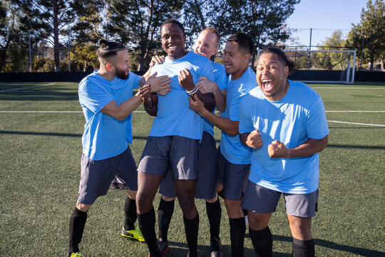 Fototapeta Soccer players wearing blue jerseys. The team is celebrating and the men are happy shouting and giving high fives after a score during a game. 