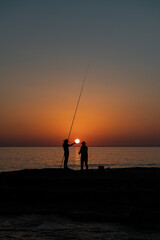 Silhouette of a girl and a man fishing with a fishing rod in the sea at sunset.