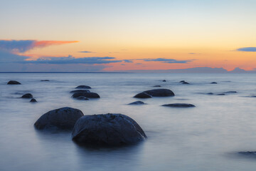 Evening at the shore of Baltic sea. Bright sunset and sea waves. Erratic boulders. Long exposure.