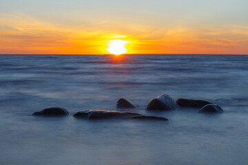 Sunset over the sea, orange strip of sunshine. Erratic boulders appearing from the water.
