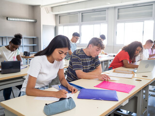 Group of diverse teenage students taking an exam in a class. Education day concept