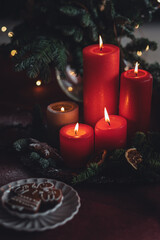Beautiful elegant table decoration with red candles, fir tree branches with handmade craft toys in the living room. Cozy home atmosphere, holiday aesthetics, atmospheric lights, gingerbread cookies