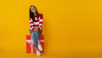 Photo of an attractive smiling young trendy woman with gift box isolated on yellow background....