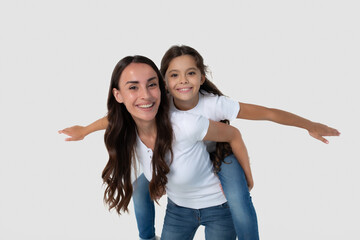 Cute smiling young brunette mother holds on back her cute little daughter in white T-shirts...