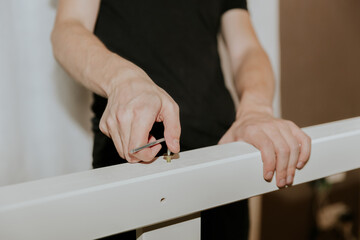 A young man uses a shaped screwdriver to tighten a screw into the side of a bunk bed.