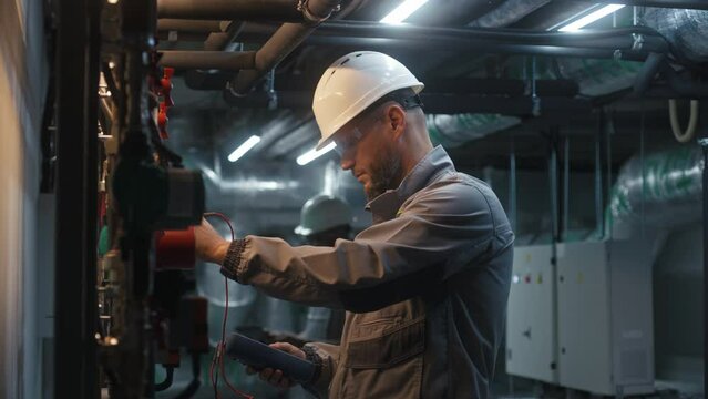 Male heavy industry worker wearing safety uniform, protective glasses and hard hat check pipes using professional equipment. Engineer maintains modern manufacturing factory or industrial facility.