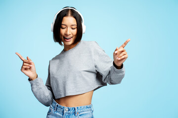 Beautiful smiling Asian woman hipster listening to music in headphones pointing fingers, dancing