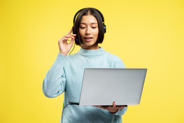 Beautiful Asian businesswoman, saleswoman holding laptop, wearing headphones talking, answering call