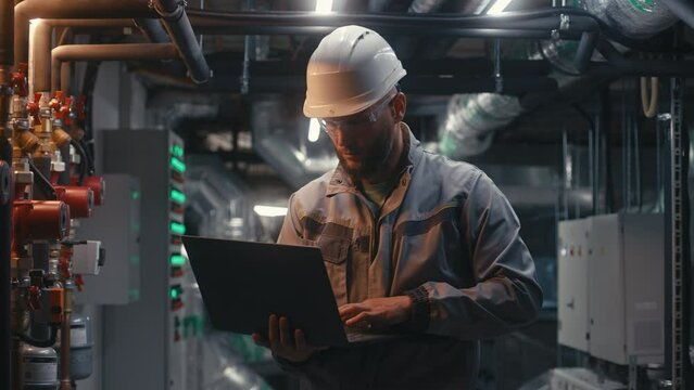 Multiethnic team of factory specialists work on modern factory using laptop and tablet computers. Heavy industry workers wearing safety uniform and hard hat check pipes. Industrial energy facility.