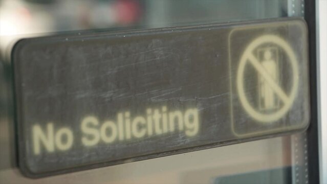 no soliciting horizontal sign on glass window with reflection of vehicle car passing with illustration picture of person crossed out, white and black