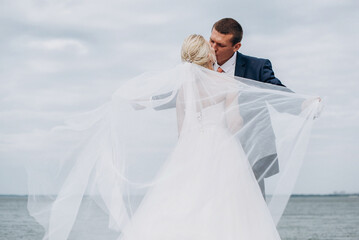 Portrait of a bride and groom on a background of sea, rocks and sky. The newlyweds are hugging.