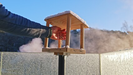 Caucasian Male Refilling Bird Feeder with Seeds Cereal and Grains on Cold Frosty Winter Day