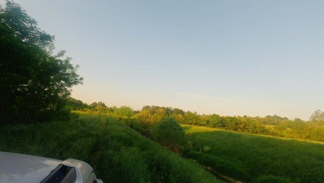 Small green hill and sunlight trees captured from car roof in blue sky in Ub, Serbia