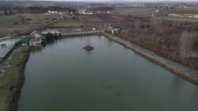 Small island in the middle of a lake and few houses and fields in background in cloudy day