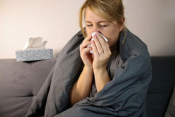 Close up of sick woman sneezing in a tissue at home