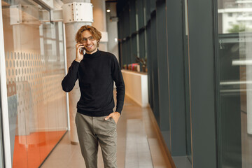 Handsome male freelancer in eyeglasses is talking phone standing in modern coworking space