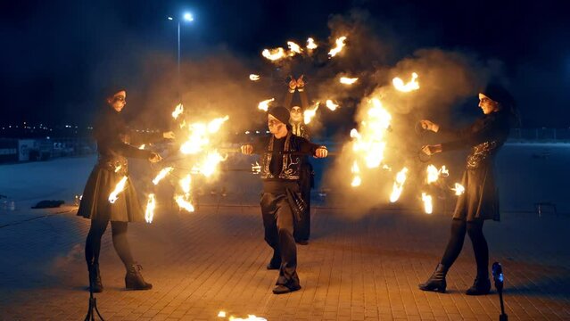 Group of four dancers move turning the burning props. Fire show performance at night outdoors.