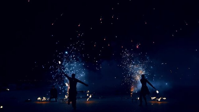 Firework show by artistic trio outdoors. Fantastic fireworks are produced by dancers at night.