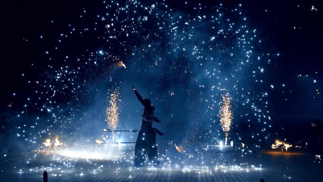 Beautiful dazzling fire show at night. Male performer dances with props producing bright sparkles.