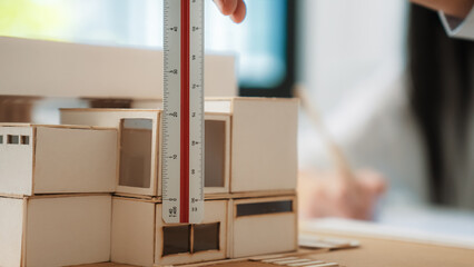 Closeup image of skilled professional engineer hand using ruler measures house model on table with...