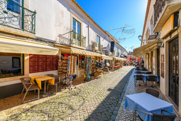 A picturesque tiled street of shops and sidewalk cafes in the historic old town center of seaside Lagos, Portugal, in the Algarve region of Southern Portugal.  - obrazy, fototapety, plakaty