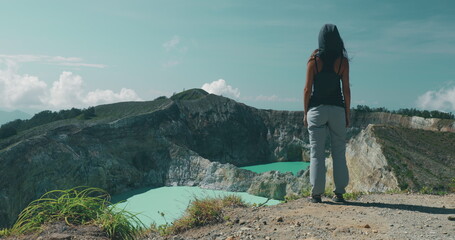 Woman tourist walking to Kelimutu blue crater lakes mountain edge. Back view of long hair girl in...