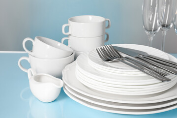 Set of clean dishes, glasses and cutlery on light blue table, closeup